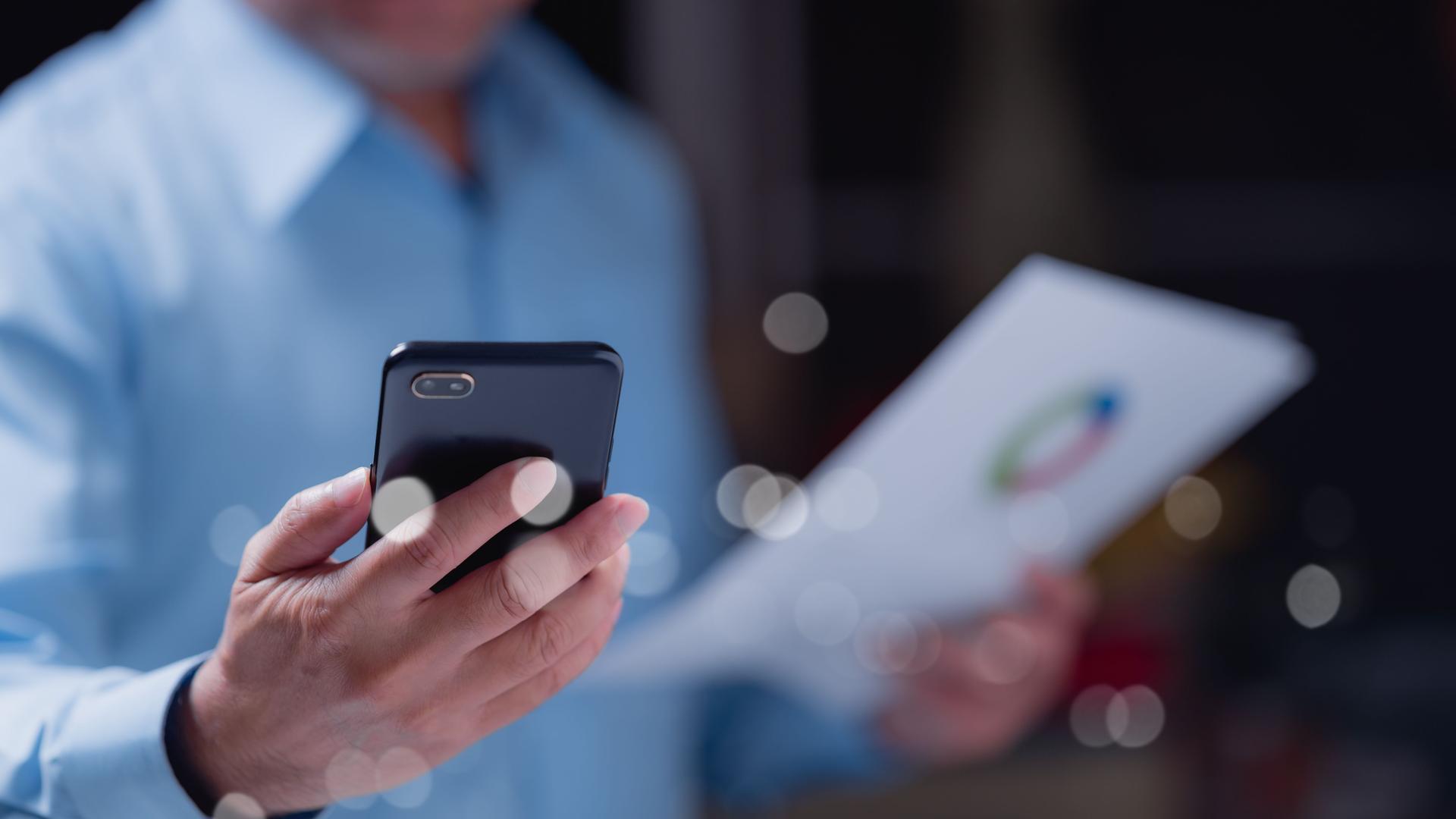 Focused individual uses their smartphone while reviewing important documents, highlighting balance between technology and work in todays fast-paced environment