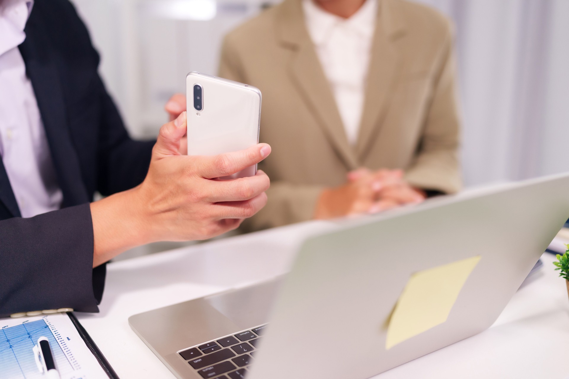 Adult Asian business professionals collaborate in office meeting using smartphone and laptop for digital communication and data exchange productivity